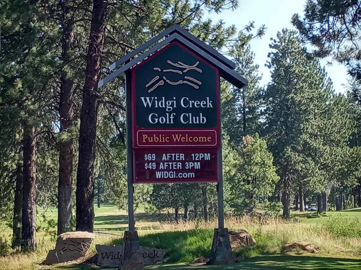 The sign for Widgi Creek Golf Club stands at the edge of a lush, well-manicured golf course, framed by green foliage. The scene illustrates the proximity and accessibility of golf for residents, with an atmosphere of relaxation and outdoor leisure.