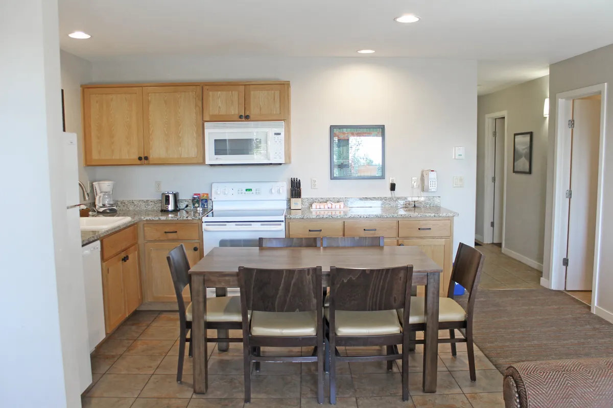 This image features a modern kitchen island, dining table, and cabinetry, all bathed in warm lighting. The space feels open and inviting, clearly designed for cooking, dining, and socializing within the comfort of a private condo.