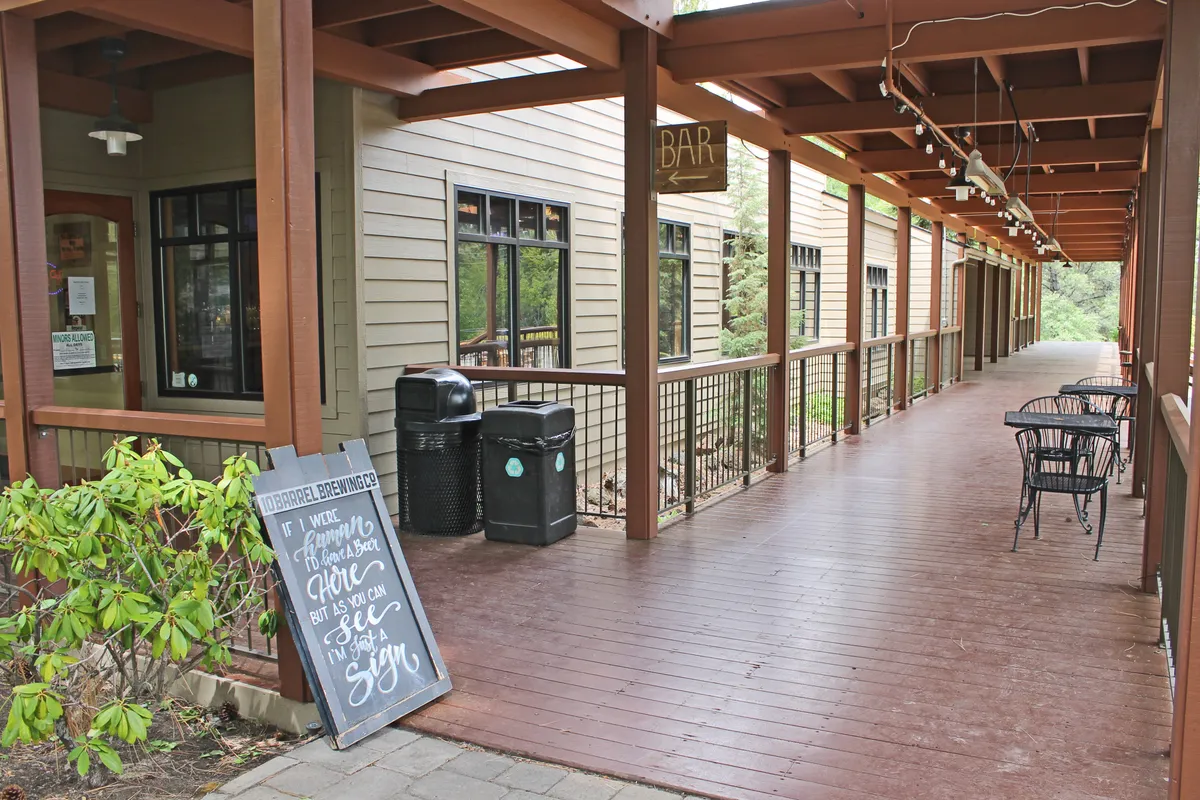 A lively exterior scene featuring a bar sign, chalkboard menu, and an outdoor seating area. The relaxed vibe suggests opportunities for casual dining, socializing, and sampling local brews, all within a vibrant, community-focused setting. The scene is animated by the possibility of live music and seasonal events, evoking the spirit of Bend's local culture.