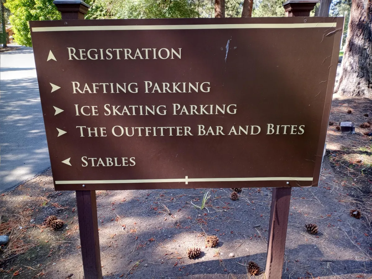 A collection of rustic signage amid towering trees points to various on-site activities, from rafting and ice skating to dining and horseback riding. The earthy, adventurous setting reflects the property’s spirit of year-round activity and excitement.