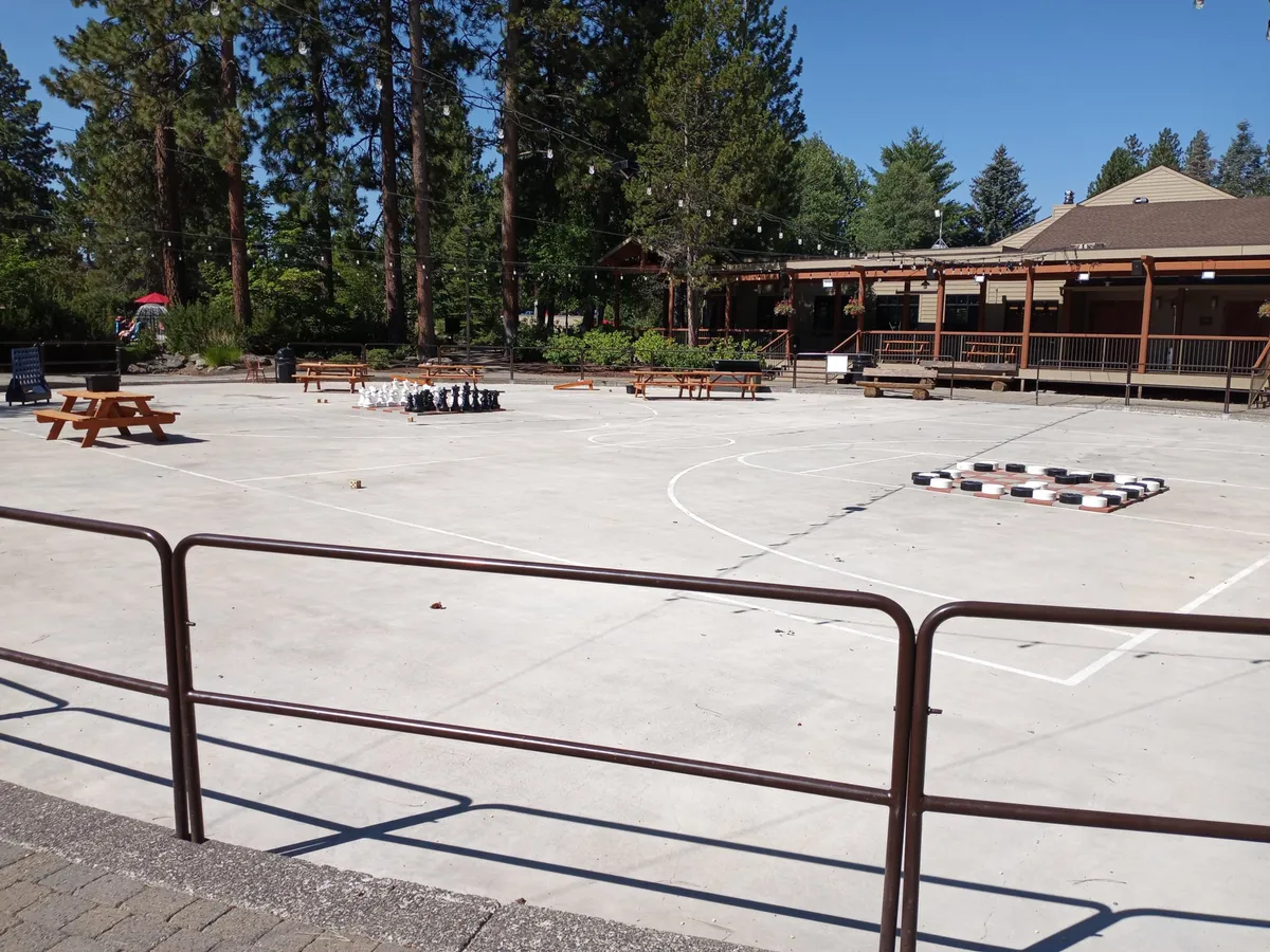 The image features a large outdoor chess set and checkers board surrounded by picnic tables and mature trees. The playful, communal setting is ideal for group activities and social gatherings, inviting guests of all ages to participate in fun, friendly competition or share a picnic outdoors.