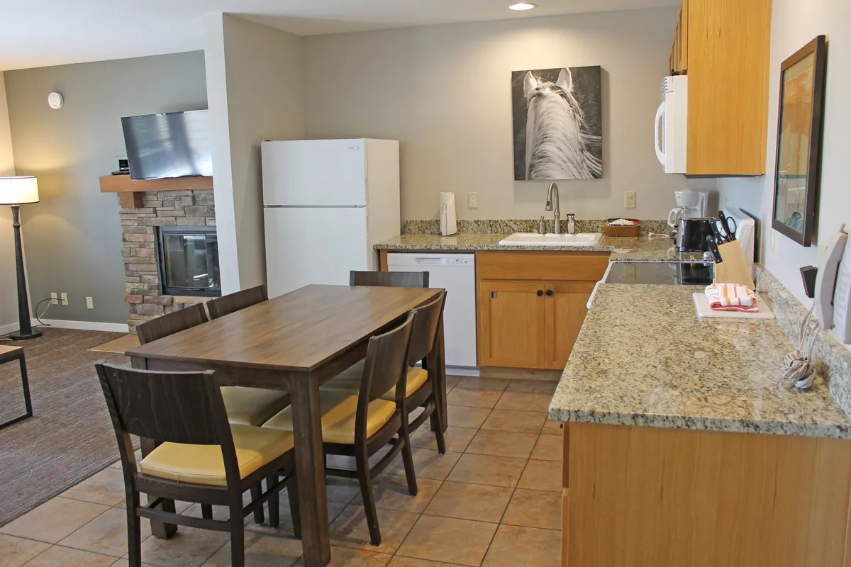 A welcoming interior shot featuring a granite-topped dining table adjacent to the kitchen, with a cozy fireplace and eye-catching horse artwork. This image spotlights the kitchen and dining zone as a social hub, ideal for meals and celebrations.