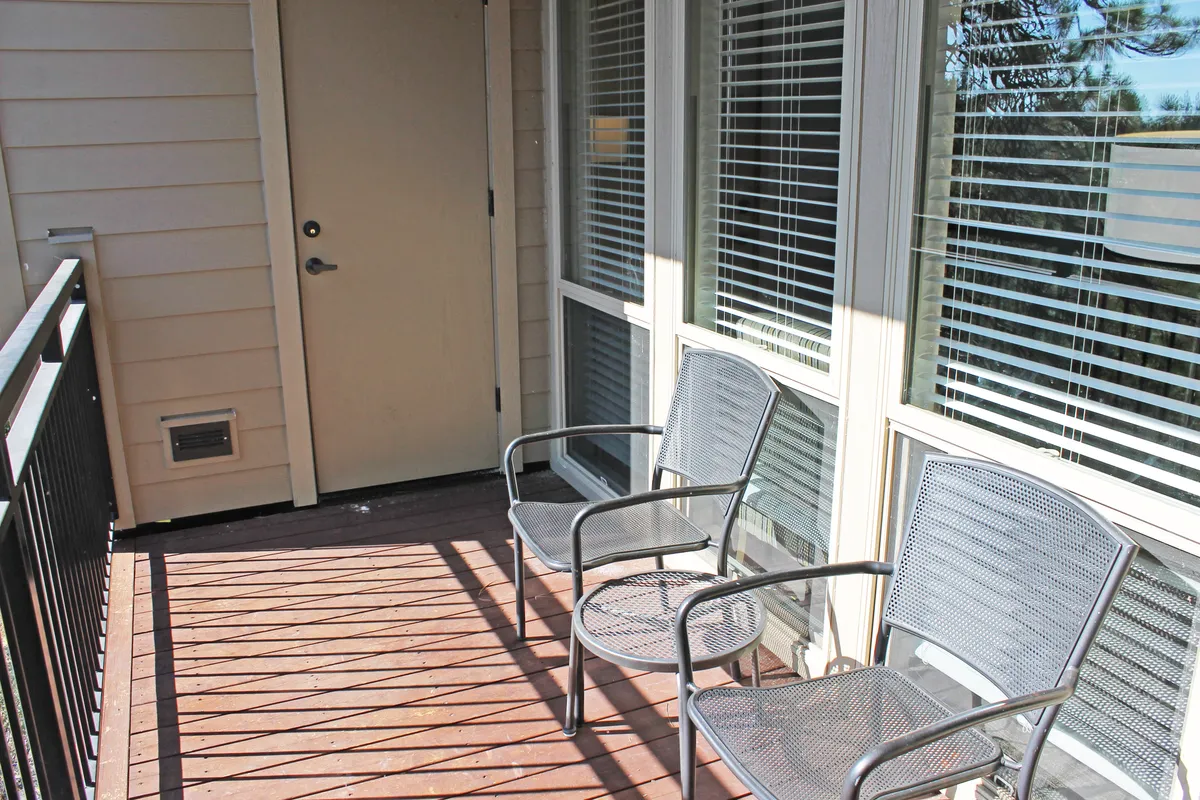 A welcoming exterior deck area with two chairs, a doorway, and a wooden deck surrounded by trees. The space is ideal for relaxing or socializing while enjoying the views and fresh air, creating a comfortable transition between indoor and outdoor experiences.