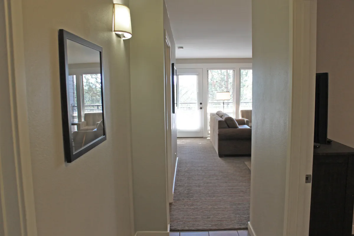 A bright, inviting corner of the living area with a comfortable sofa, a wall mirror, and natural light streaming through expansive windows. The airy layout encourages relaxation and morning coffee by the window.