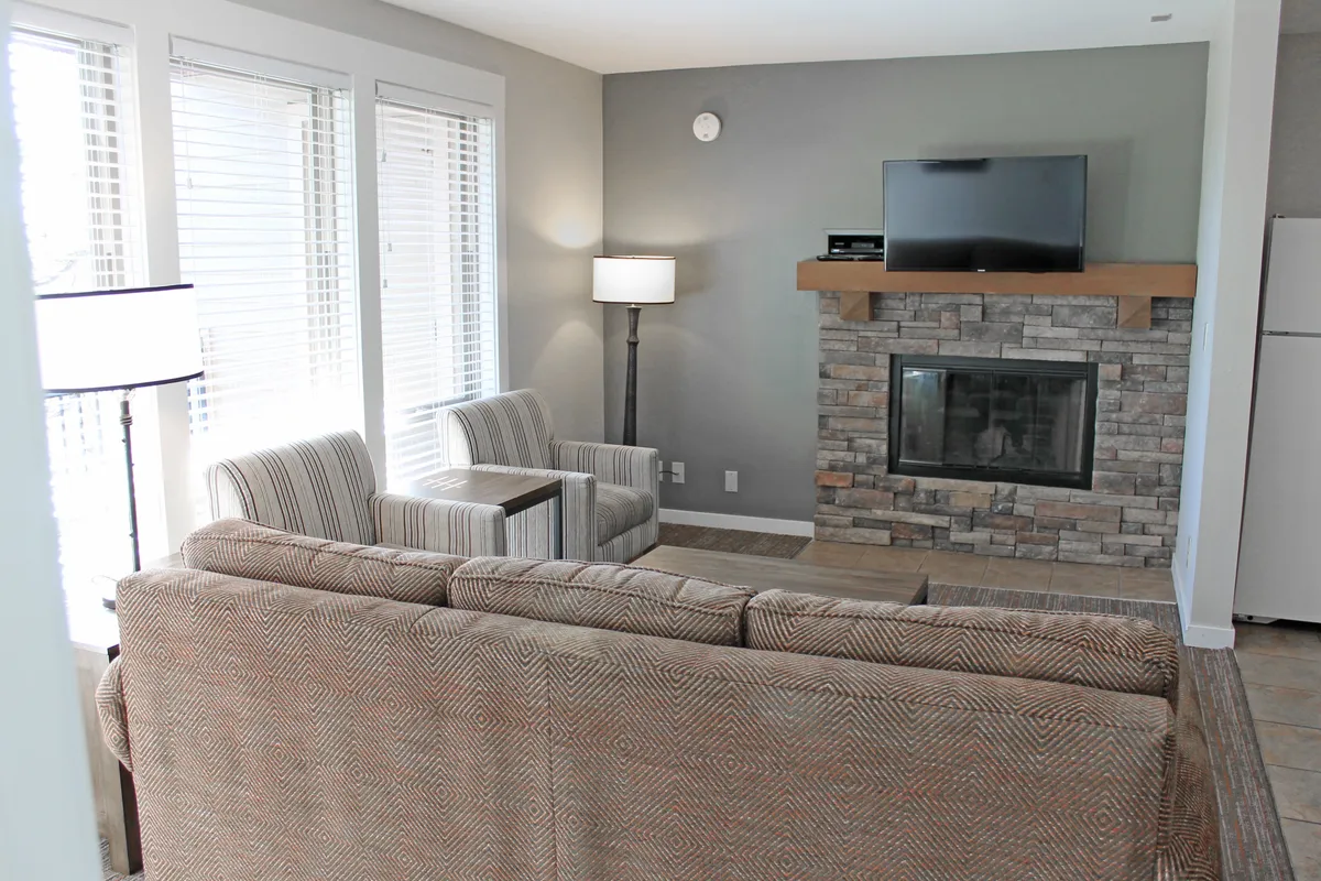 A cozy living room scene with a fireplace, television, sofa, armchairs, and large windows. The space exudes warmth, comfort, and an inviting atmosphere—ideal for relaxing after a day of resort activities.
